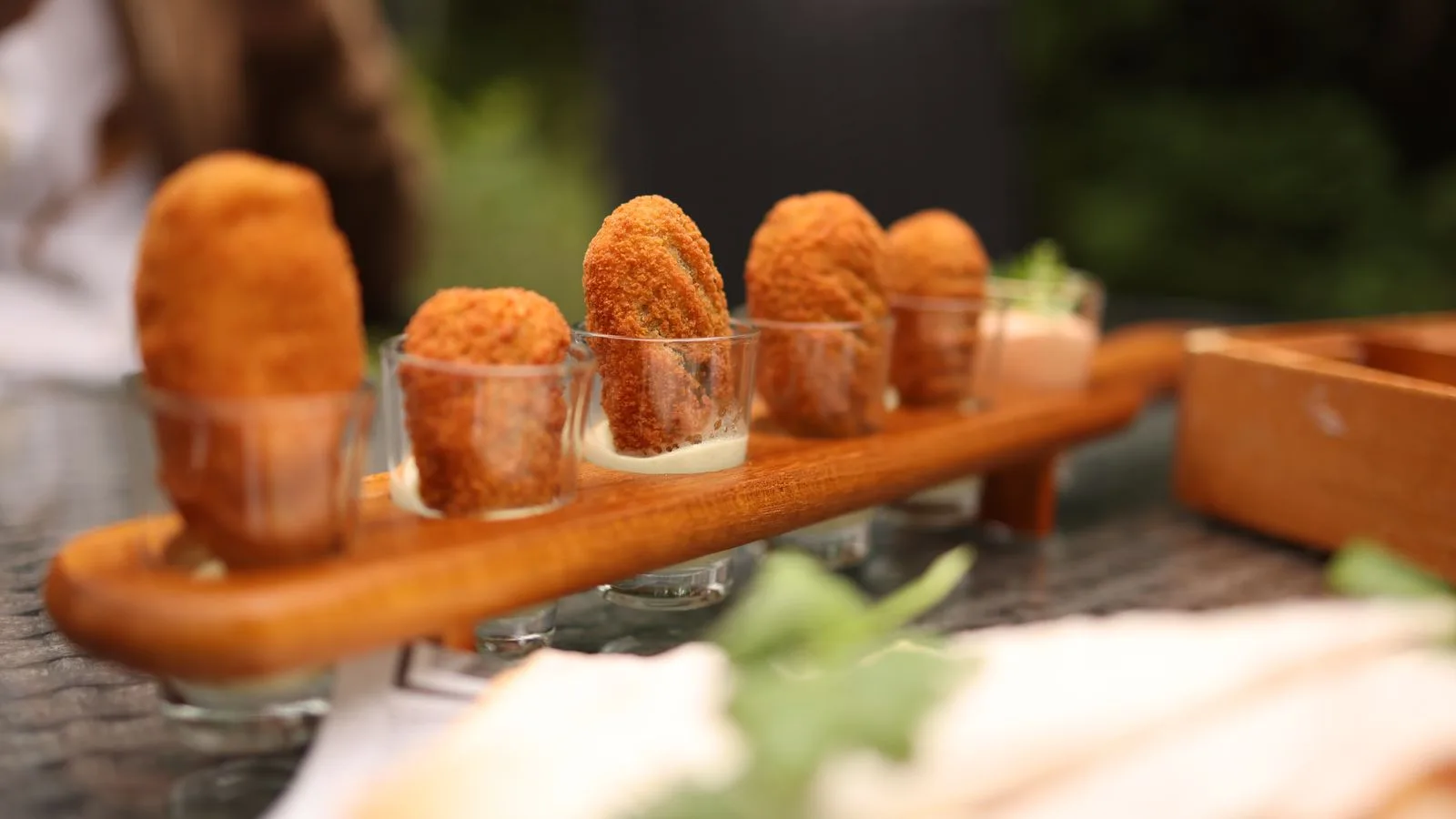 Close-up of crispy croquettes served in elegant glasses on a wooden tray, perfect for gourmet dining.