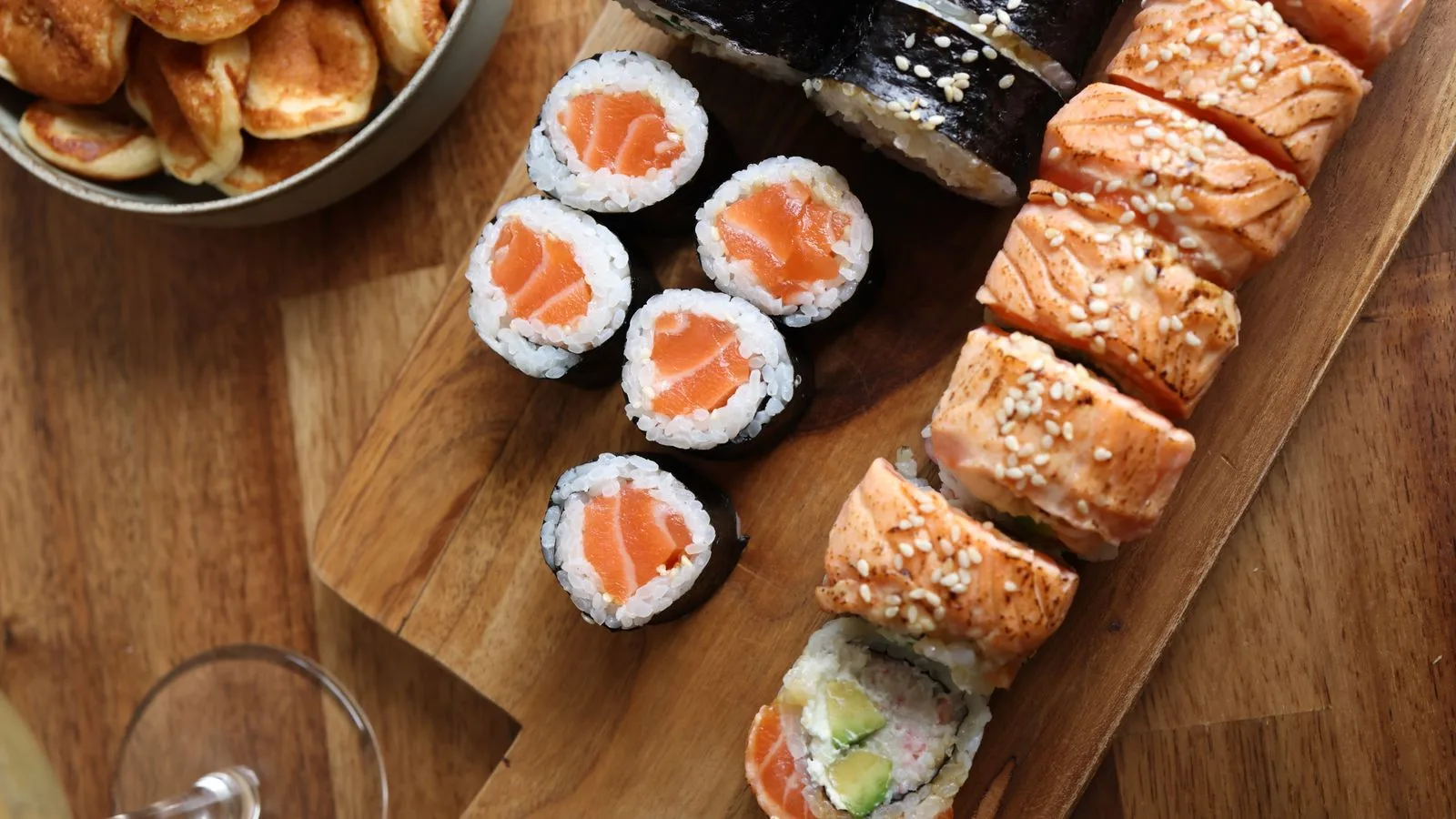 Assorted sushi rolls with salmon and sesame seeds served on a rustic wooden board.