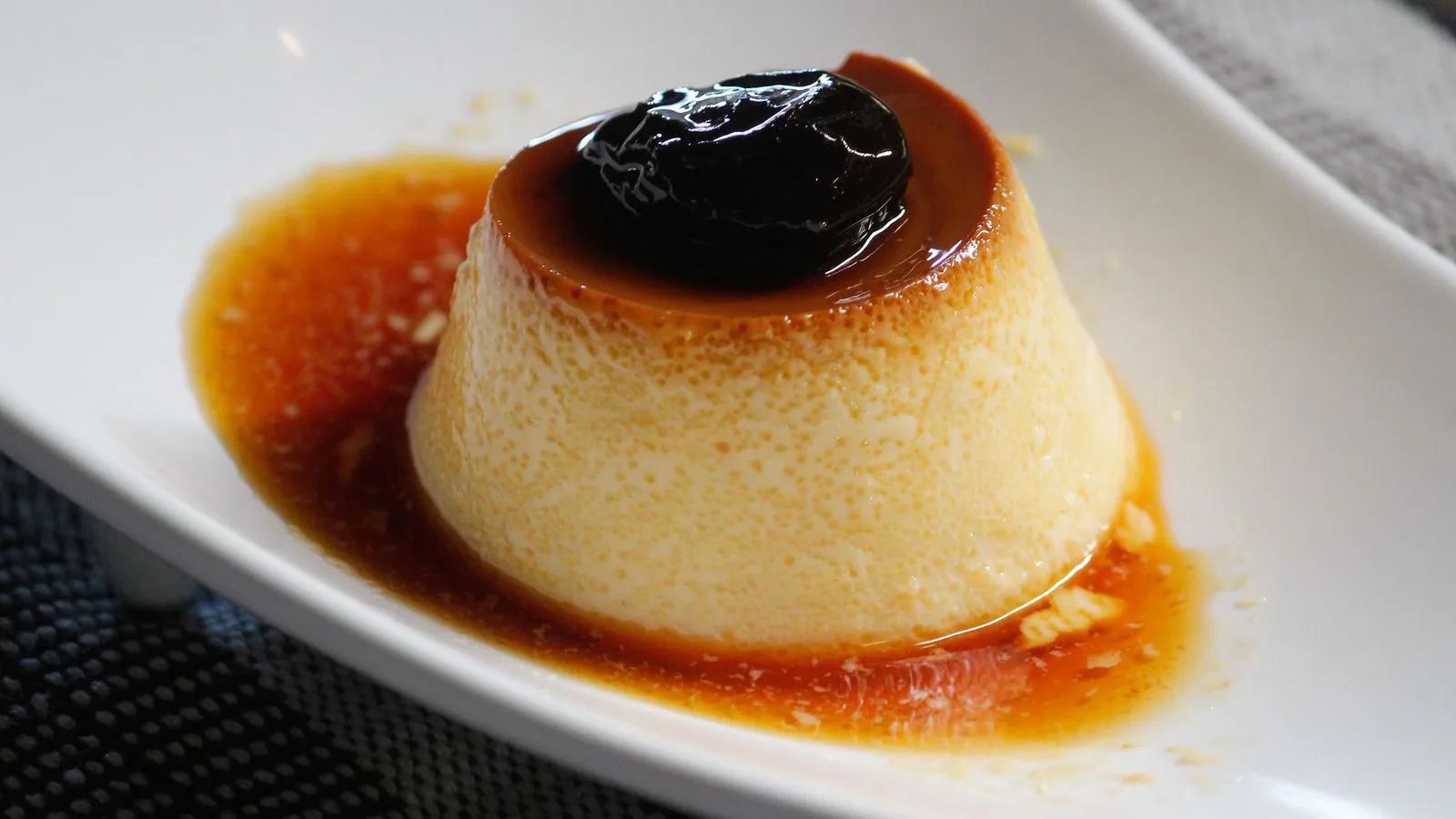 Appetizing caramel flan dessert with a rich prune topping served in a white dish.