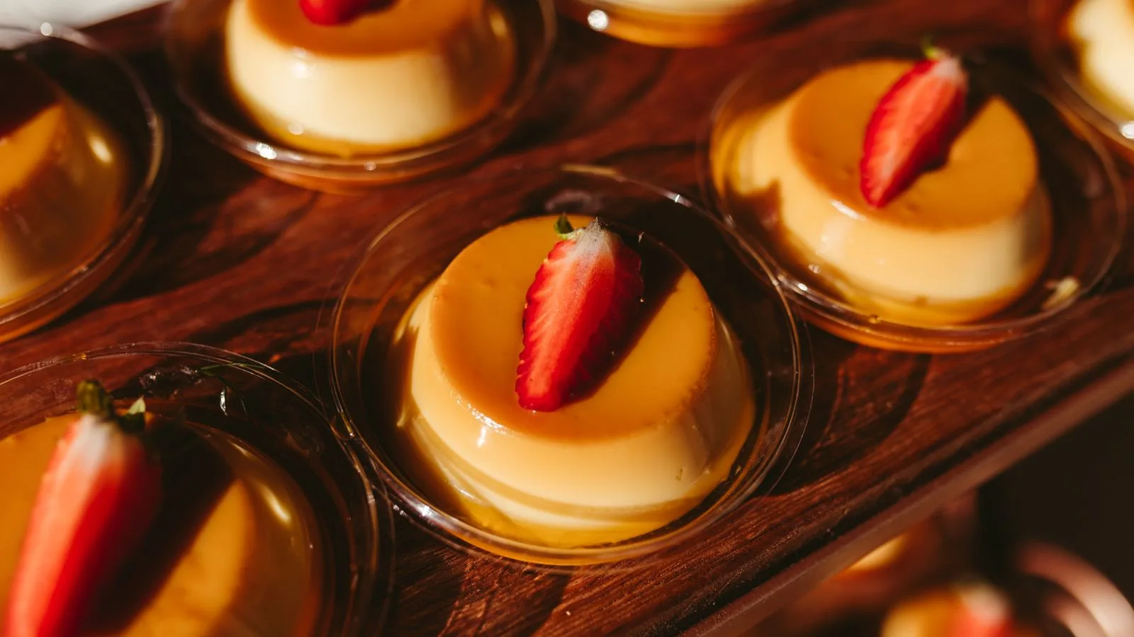 Enticing flan desserts topped with strawberries beautifully showcased on a wooden board.