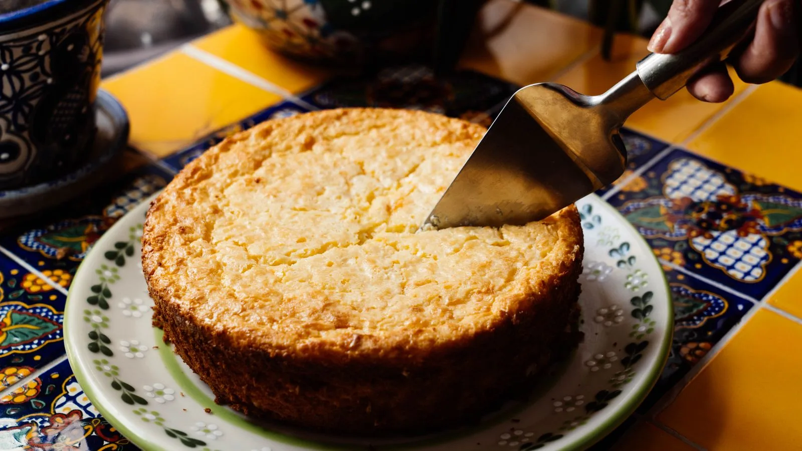 A close-up of a freshly baked Mexican cake being sliced on a colorful tiled table.