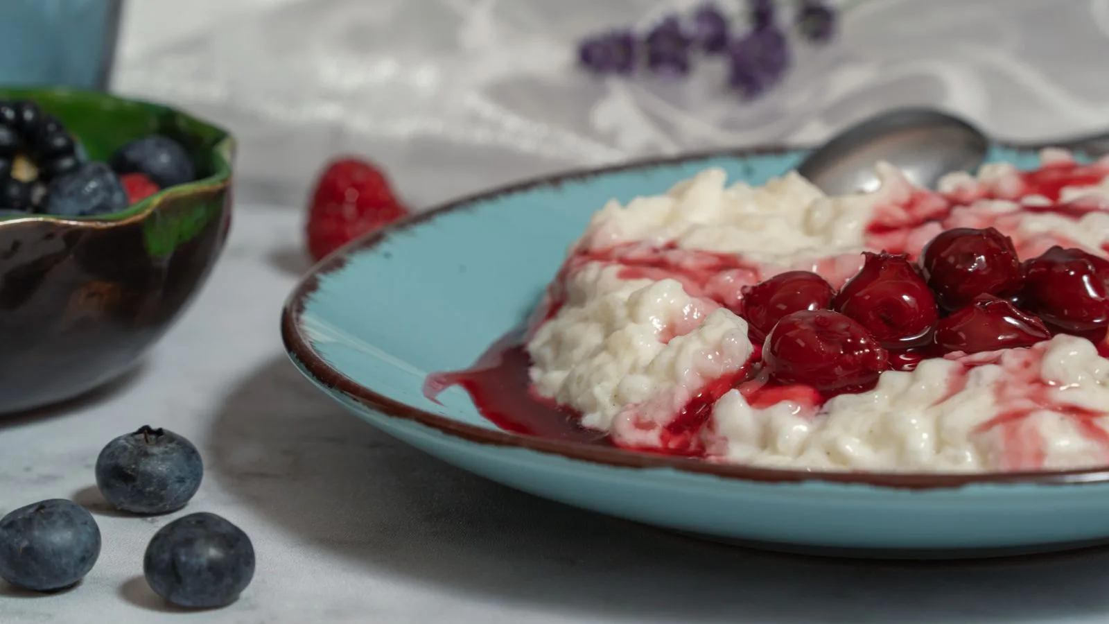Creamy rice pudding topped with cherries and surrounded by fresh berries in a cozy setting.