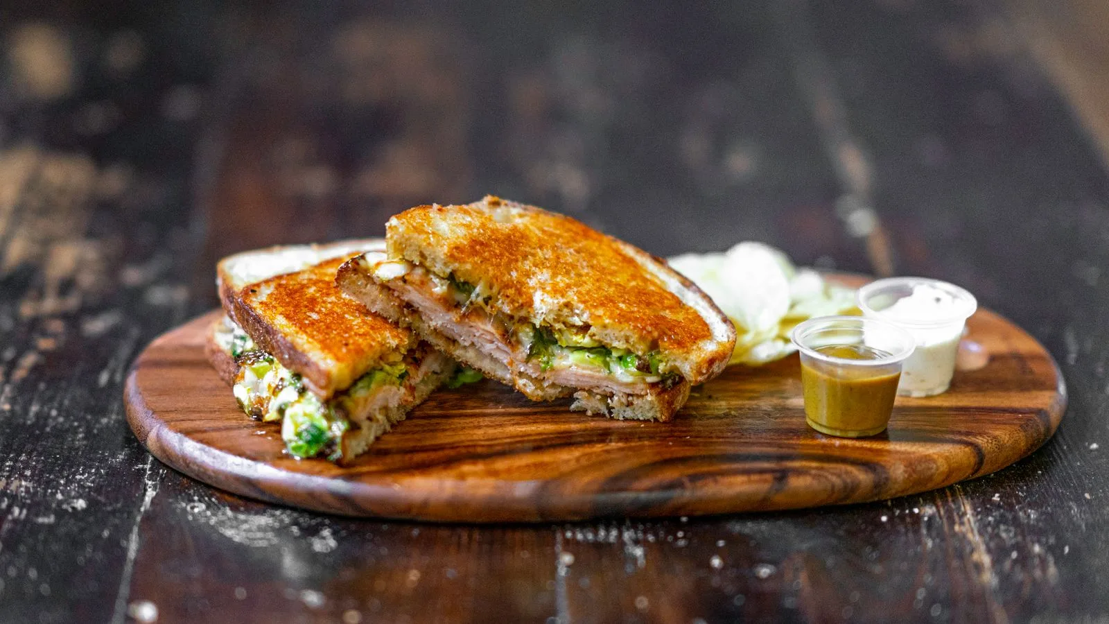 Tasty grilled ham and cheese sandwich served with dipping sauces on a wooden board.