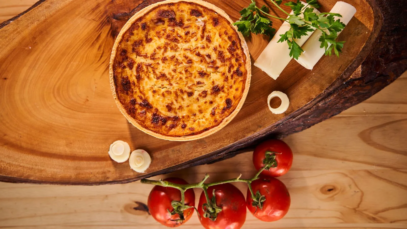 Mouthwatering cheese quiche on wooden board with tomatoes and parsley garnish, perfect for culinary themes.