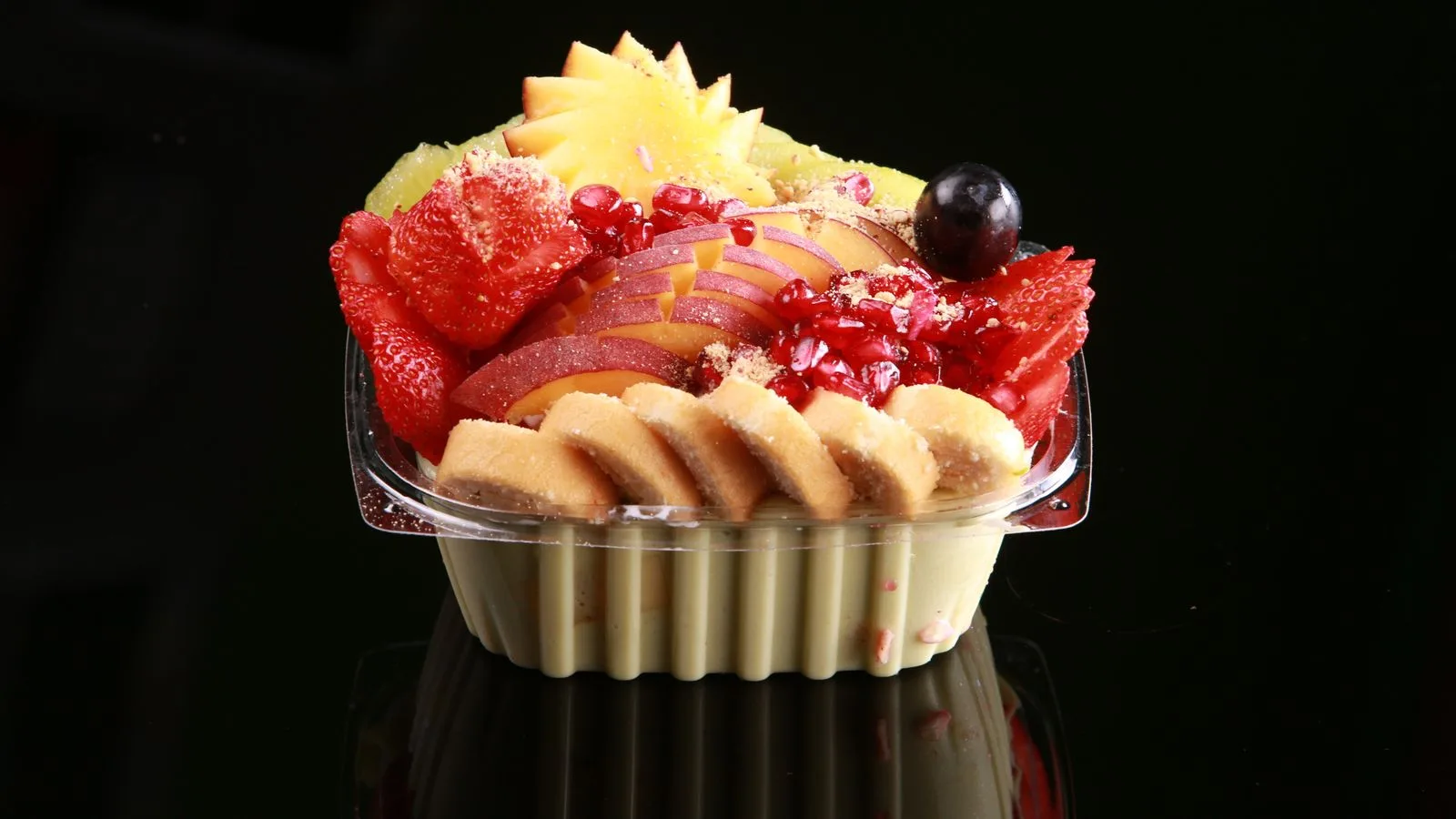 Colorful fruit salad including strawberries, bananas, and kiwis in a plastic container on black background.