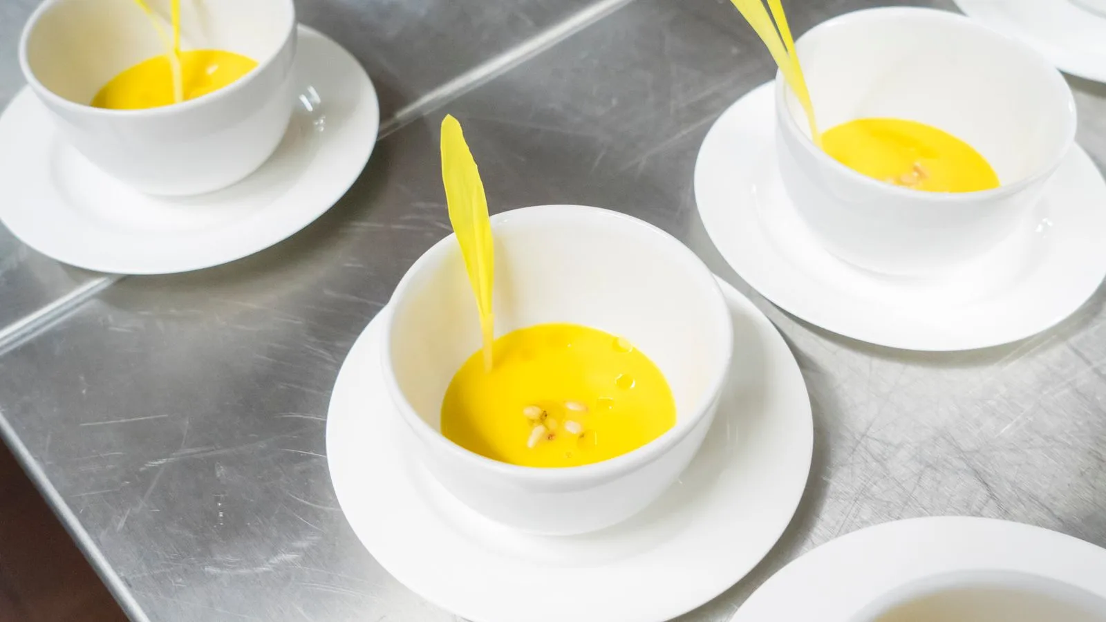 A high-angle view of creamy yellow soup garnished in elegant white bowls, exuding a modern culinary presentation.