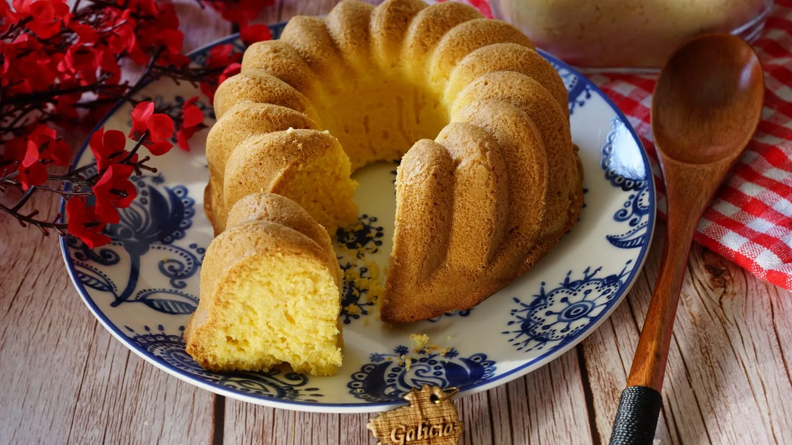 Intricate homemade bundt cake beautifully presented with red flowers on a wooden background.