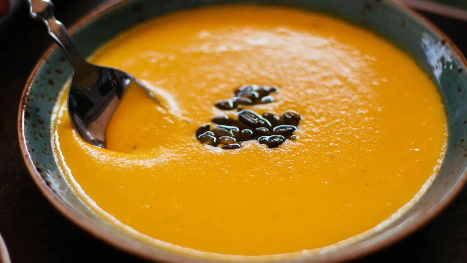 Close-up of creamy pumpkin soup with seeds in a blue ceramic bowl, perfect for a warm fall meal.
