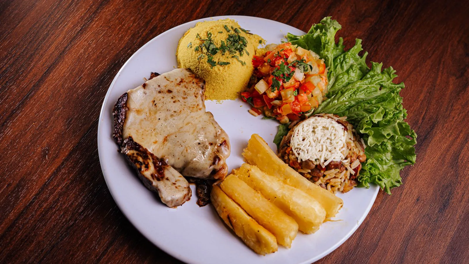 A delicious plate of Brazilian cuisine featuring pork chop, rice, beans, and fresh salad.