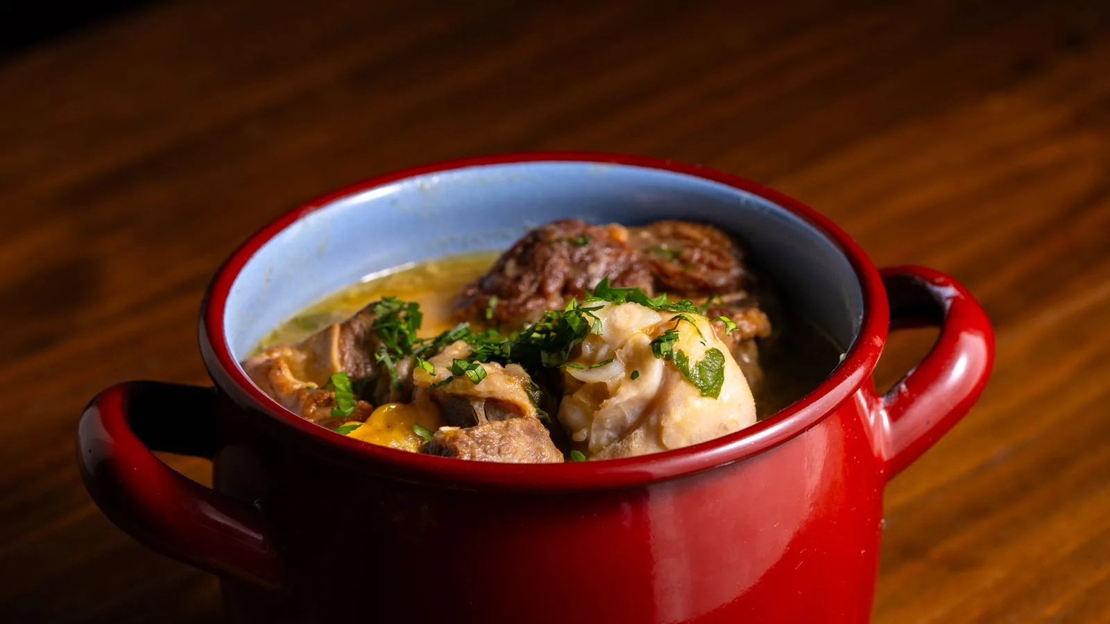 Warm and comforting hearty stew served in a rustic red pot on wood surface.