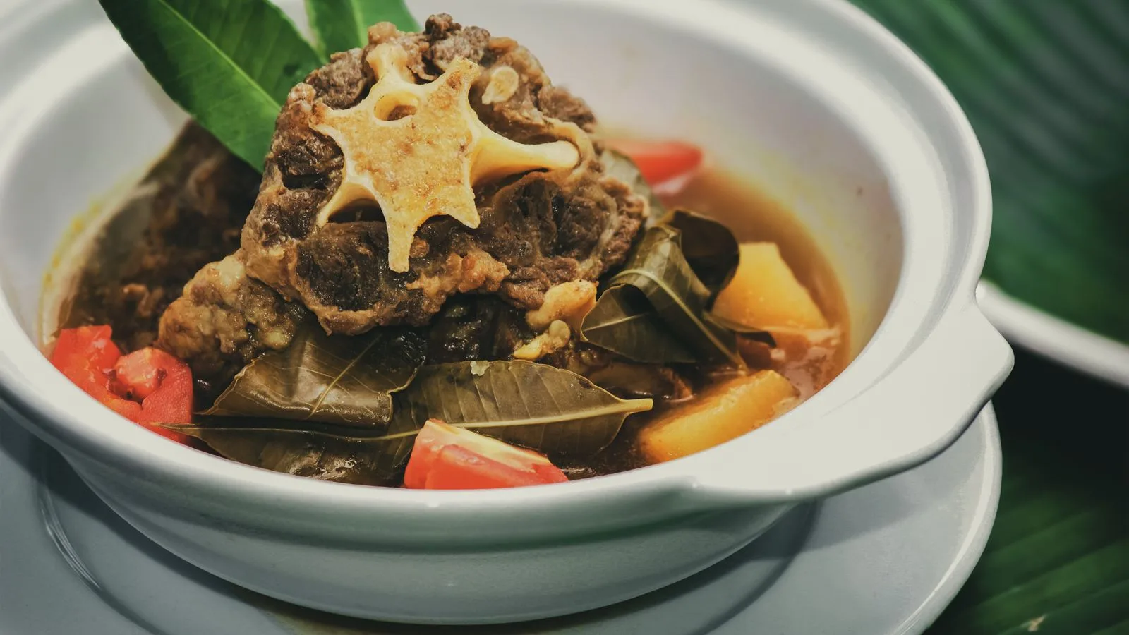 Appetizing oxtail soup from Jawa Timur, Indonesia, in a white bowl with colorful vegetables and spices.