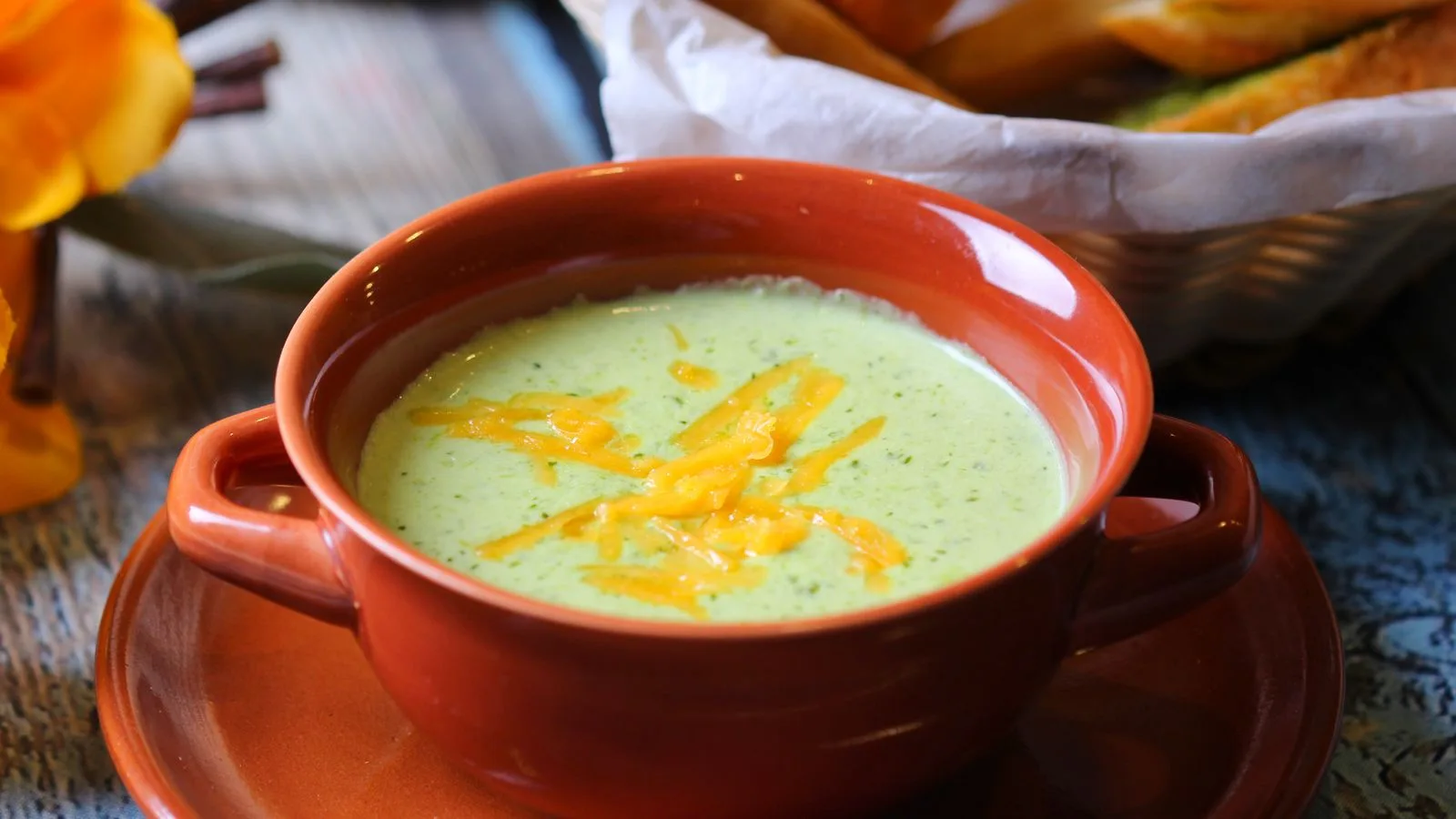 Close-up of creamy broccoli soup in a terracotta bowl with cheddar garnish.
