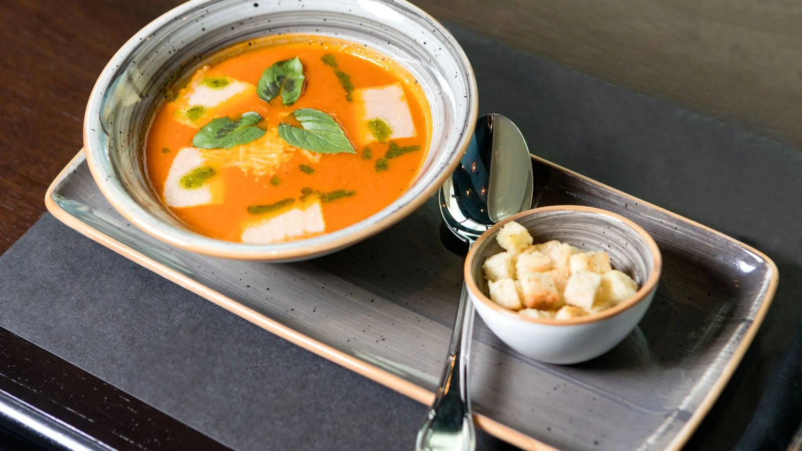 A delicious bowl of pumpkin soup served with croutons, garnished with basil leaves.