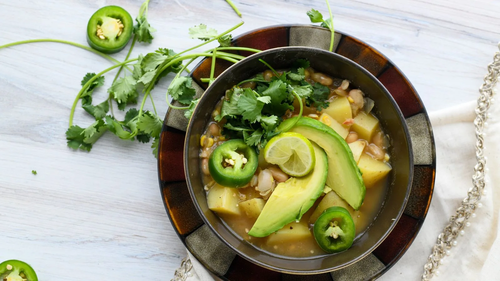 Top view of a colorful vegetable soup garnished with avocado, jalapeño, and cilantro.