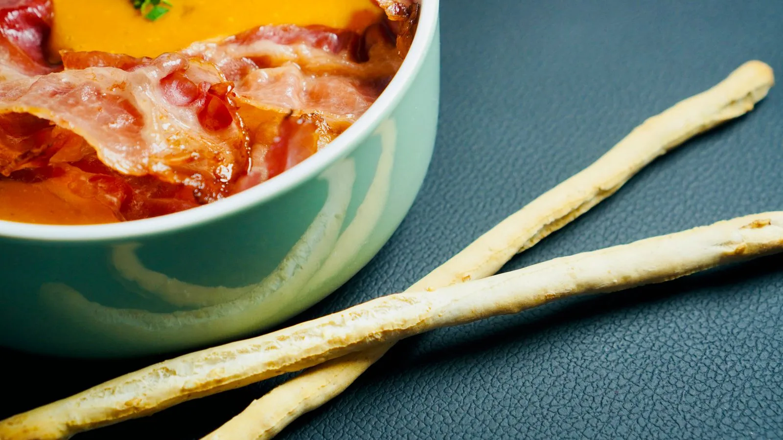 Delicious creamy soup topped with crispy bacon, accompanied by crunchy breadsticks.