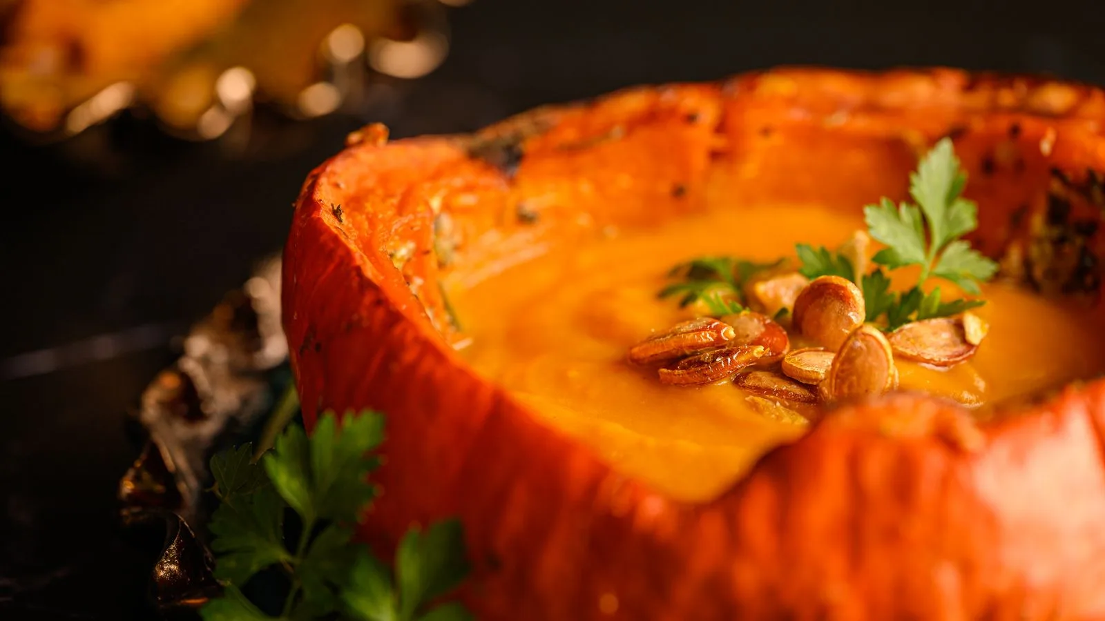 Close-up of creamy pumpkin soup garnished with seeds and parsley in a pumpkin bowl.
