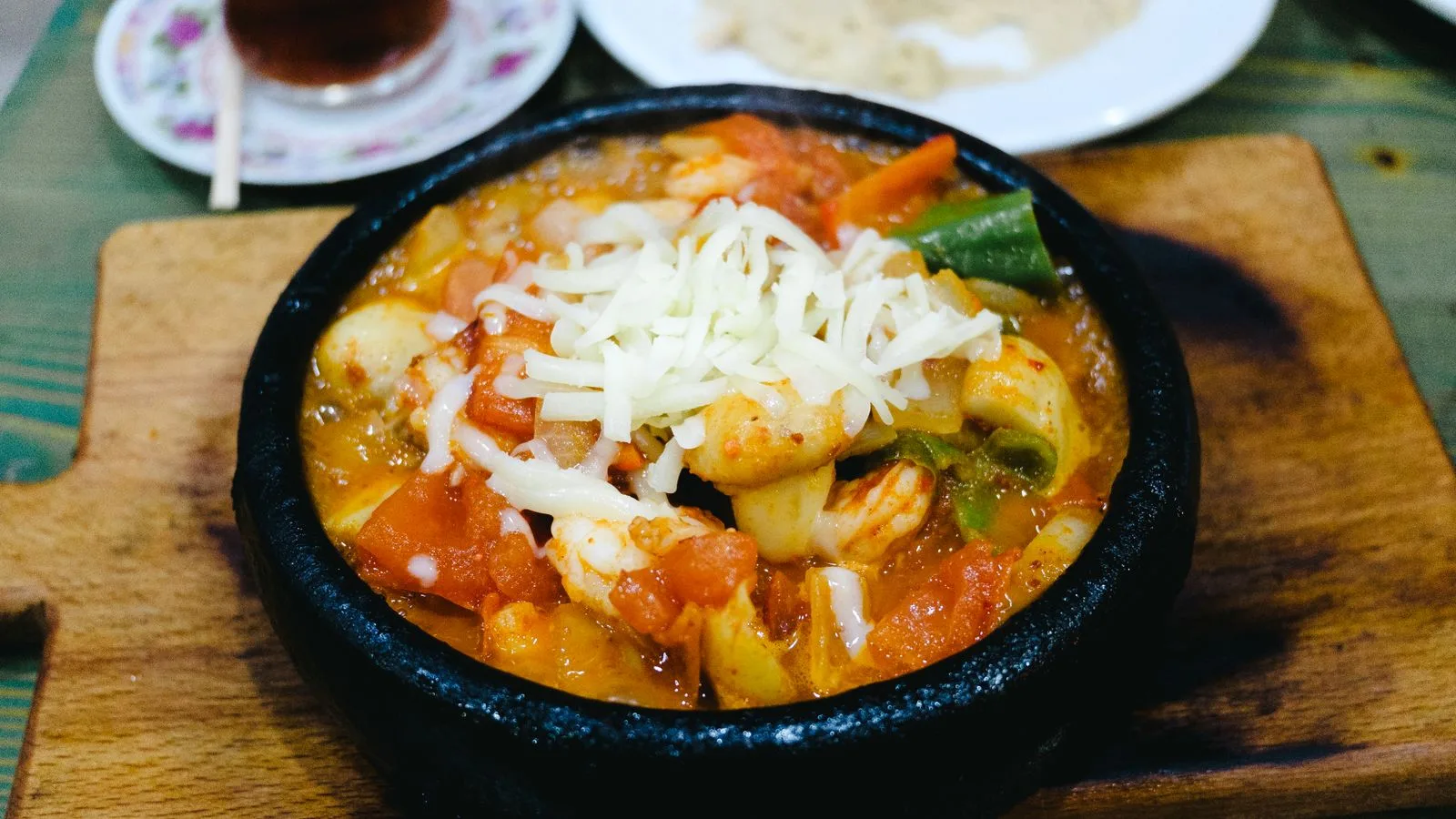 Savory shrimp and vegetable casserole topped with cheese, served on a rustic wooden board.