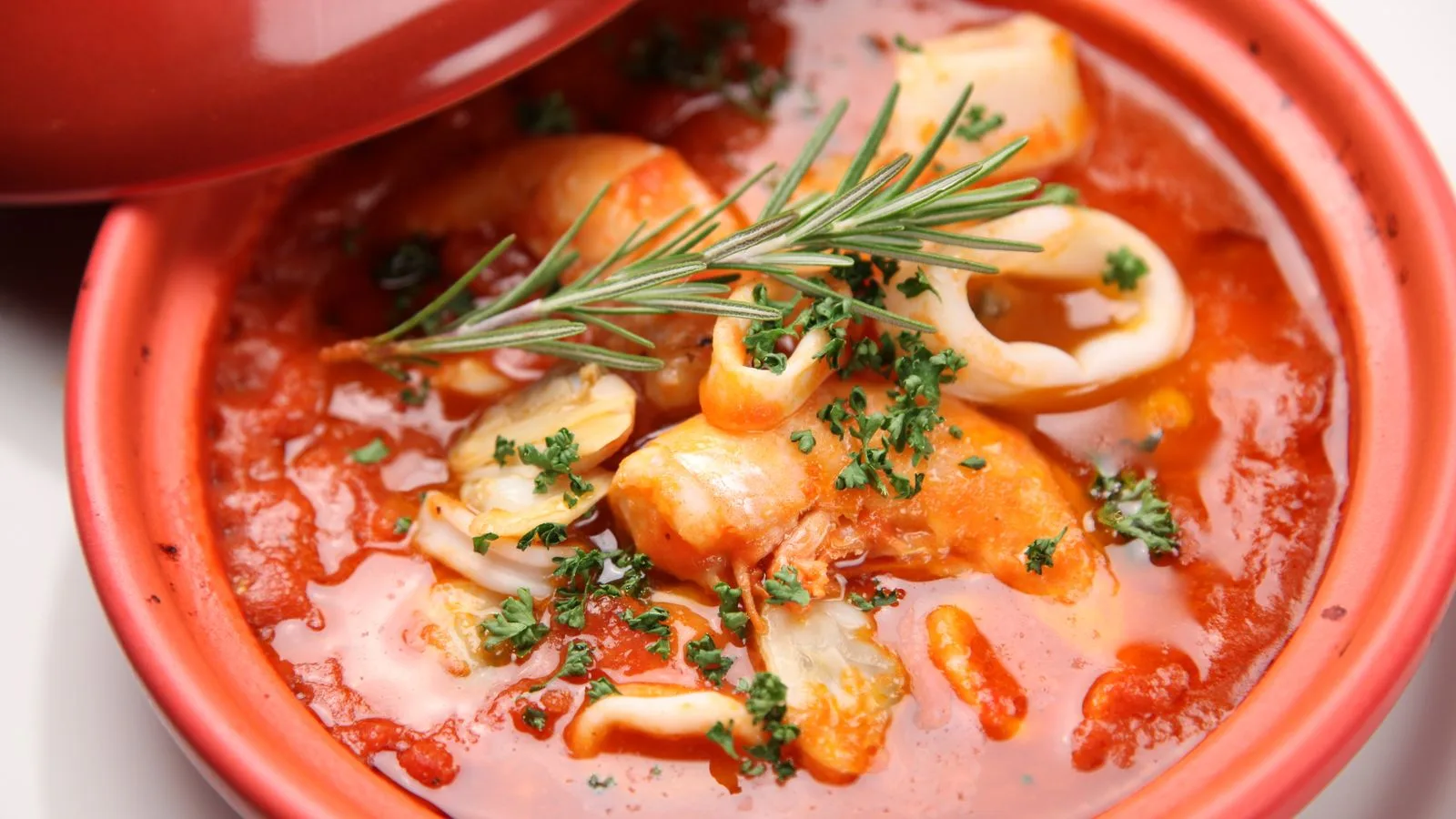 A warm seafood stew with herbs and vibrant tomato sauce served in a ceramic bowl.