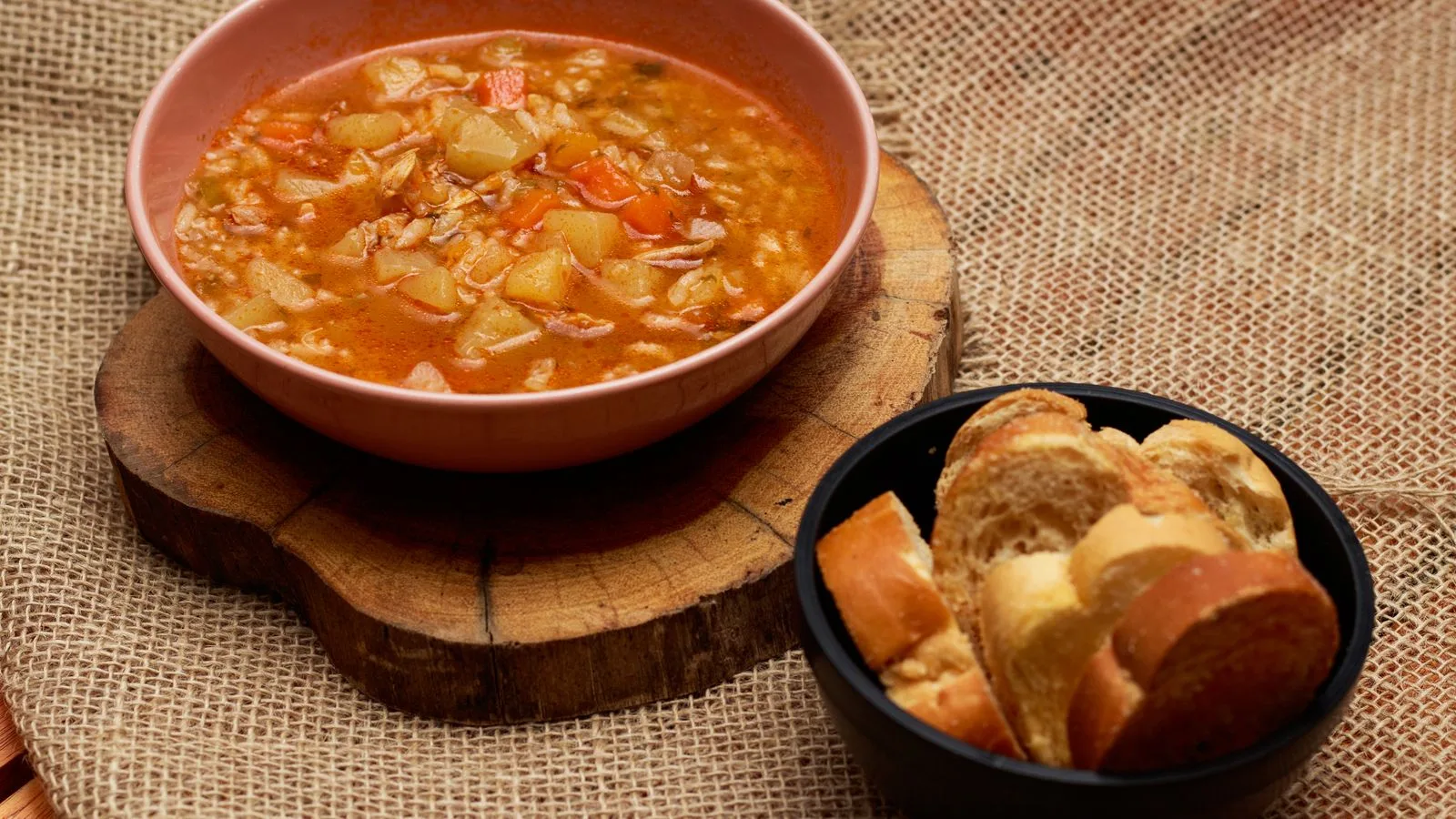 Warm vegetable soup and bread served on rustic surface, perfect for cozy meals.