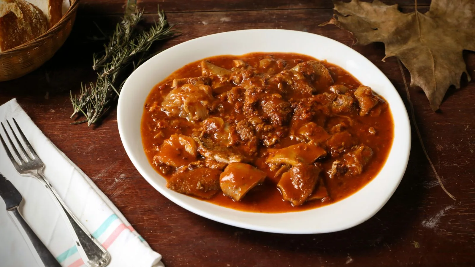 Hearty Italian tripe stew served with bread and herbs on a rustic wooden table.