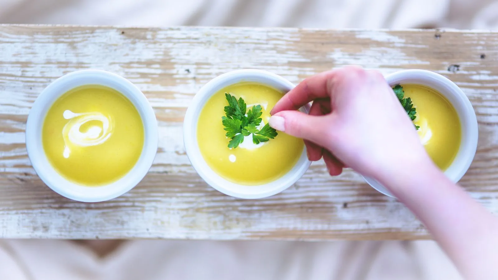 Hand adding garnish to creamy soup bowls, perfect for lunch or dinner.