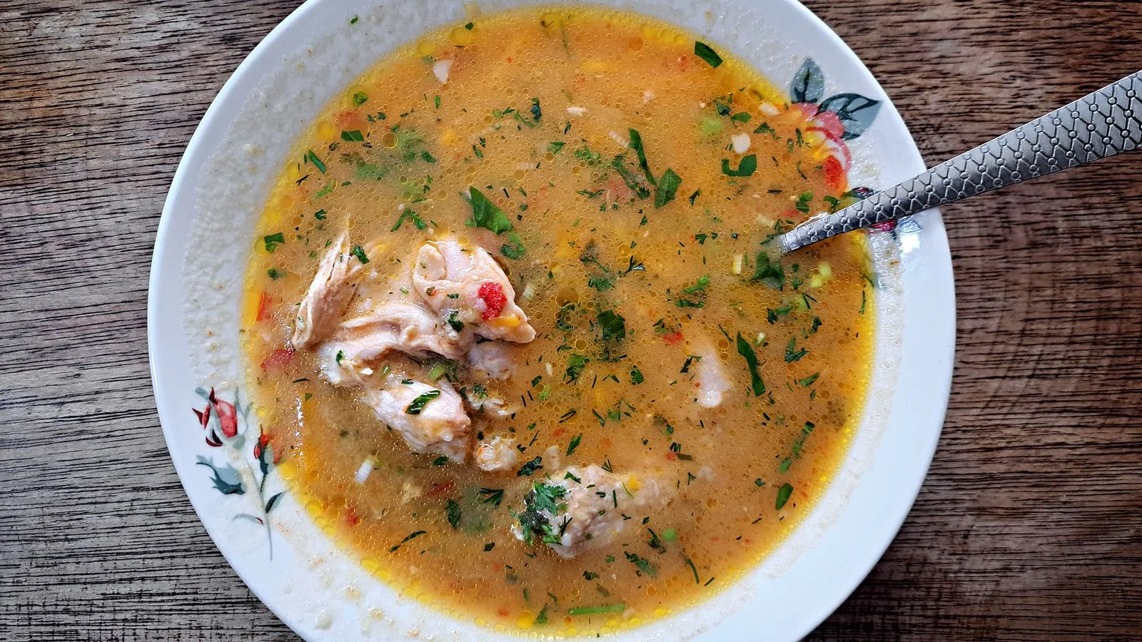 A top view of traditional Ecuadorian fish soup in a floral bowl with herbs on a wooden table.