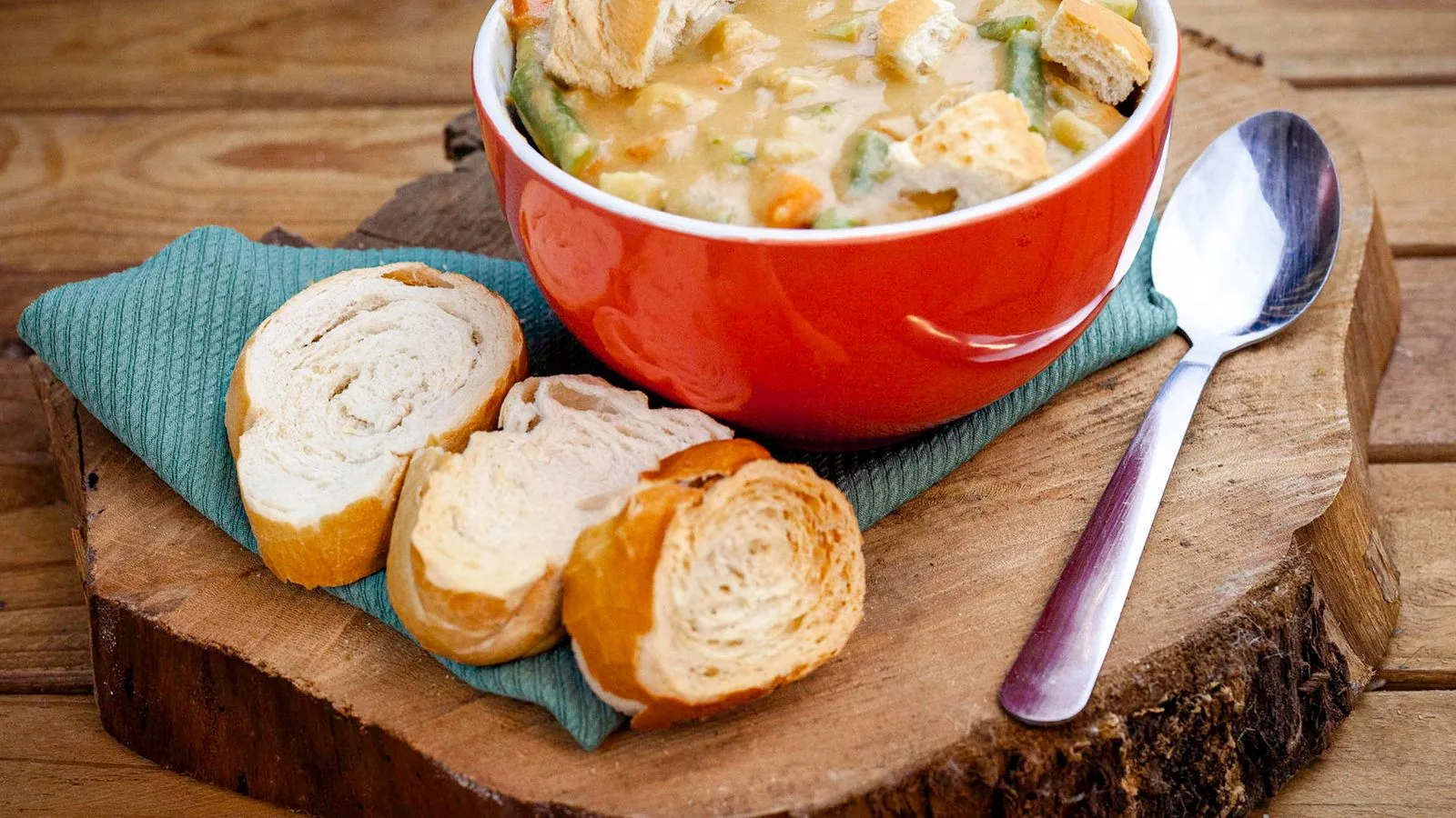 Warm vegetable soup in vibrant red bowl with crusty bread slices on wooden board. Perfect cozy meal.