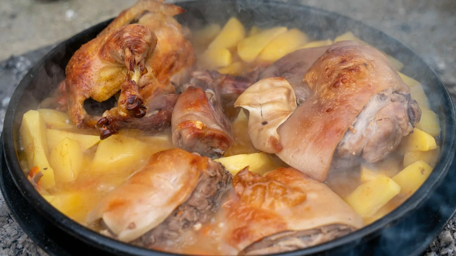 A mouth-watering close-up of braised chicken and pork with potatoes in a hot pan.