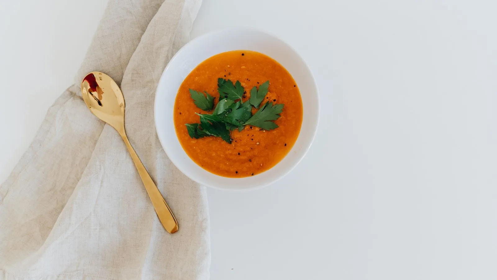 Elegant bowl of carrot soup garnished with fresh herbs on a white background.