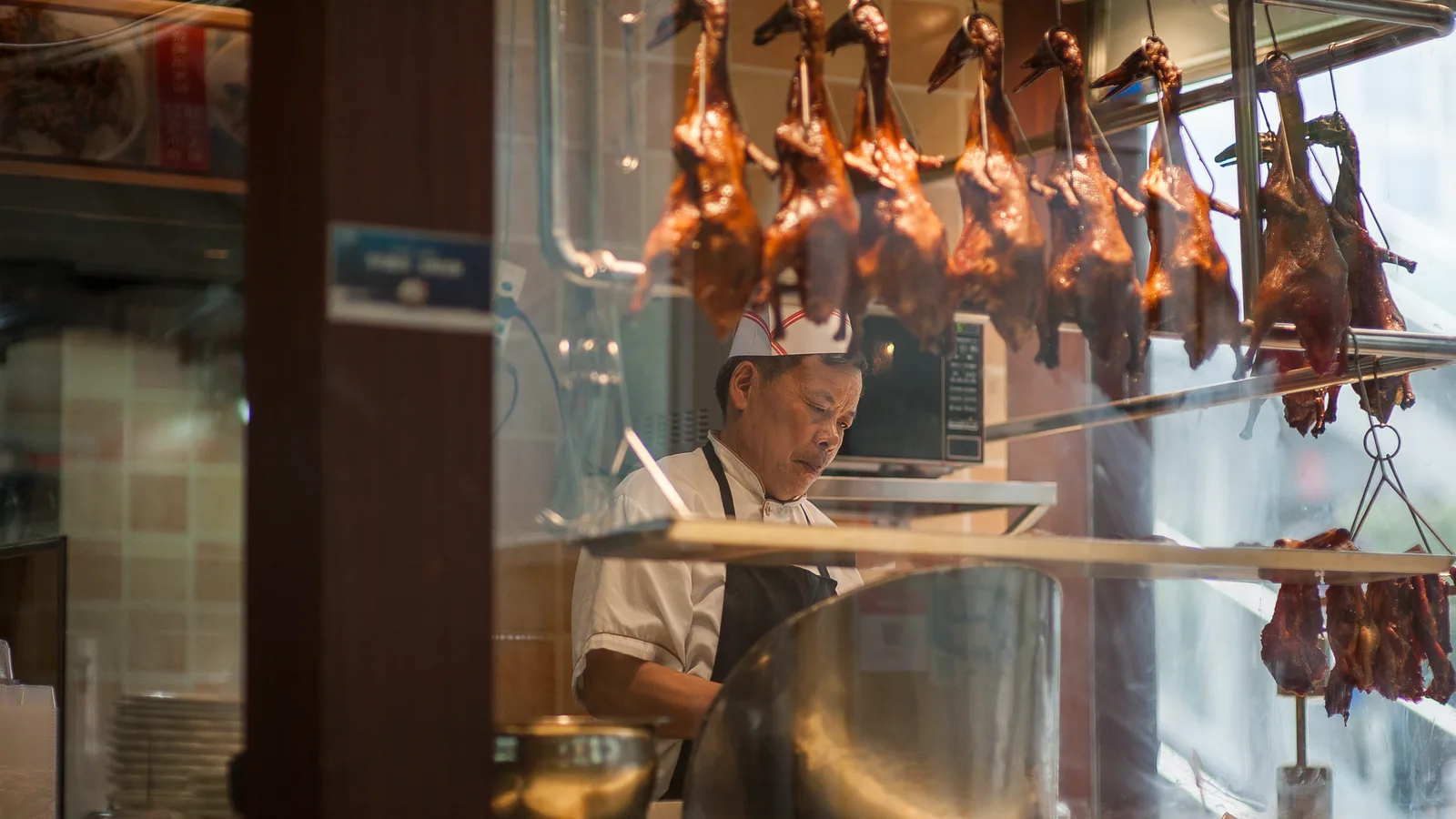A chef in a traditional Asian restaurant prepares roasted duck, displaying culinary skills.