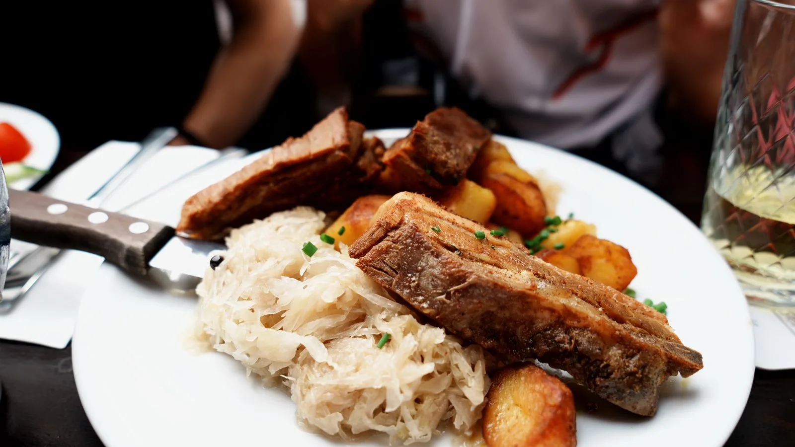 Plate of roast pork ribs, sauerkraut, and potatoes served in a cozy setting.