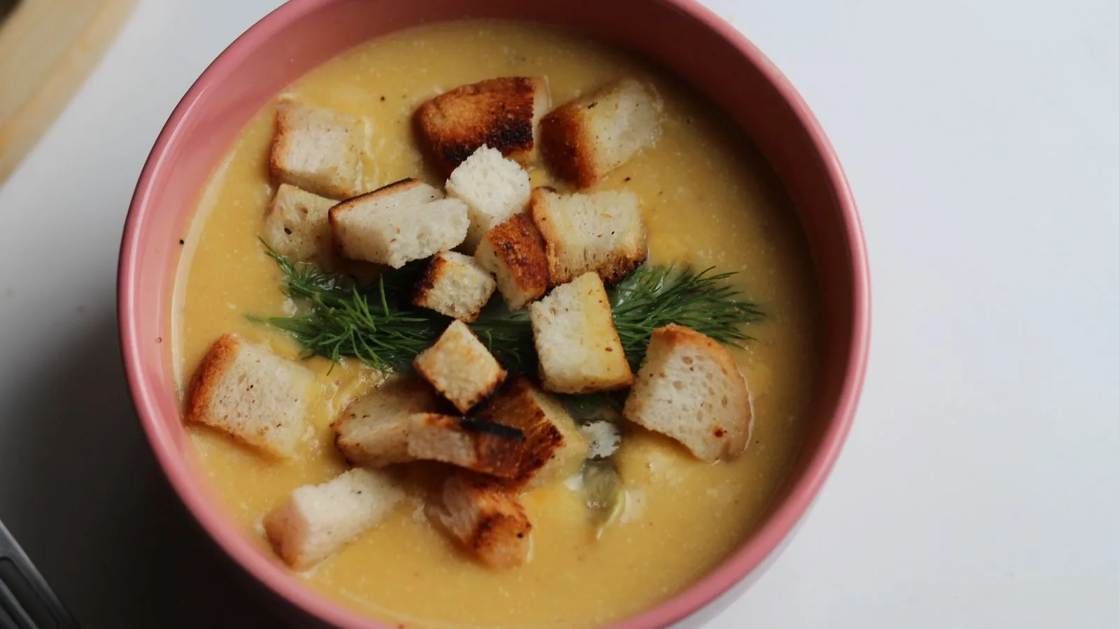 Delicious creamy pumpkin soup topped with crispy croutons in a pink bowl.