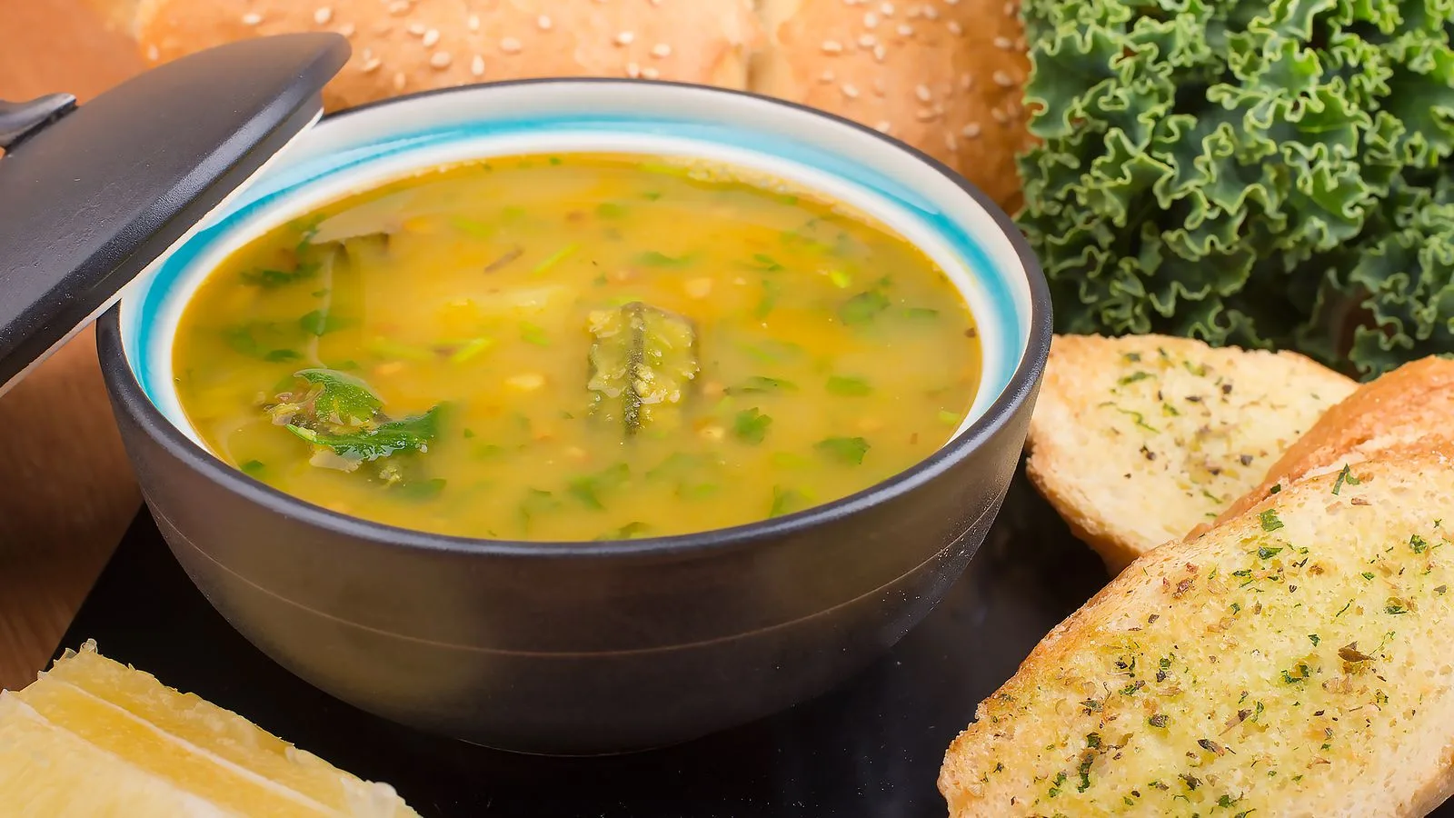 Delicious bowl of vegetable soup served with garlic bread and fresh greens.