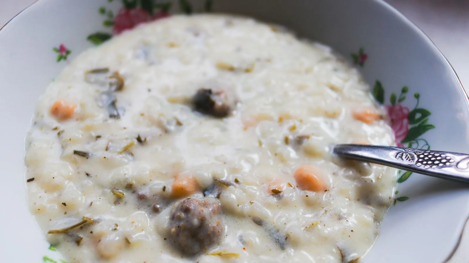 A close-up of a creamy vegetable and meat soup in a floral bowl with a spoon.