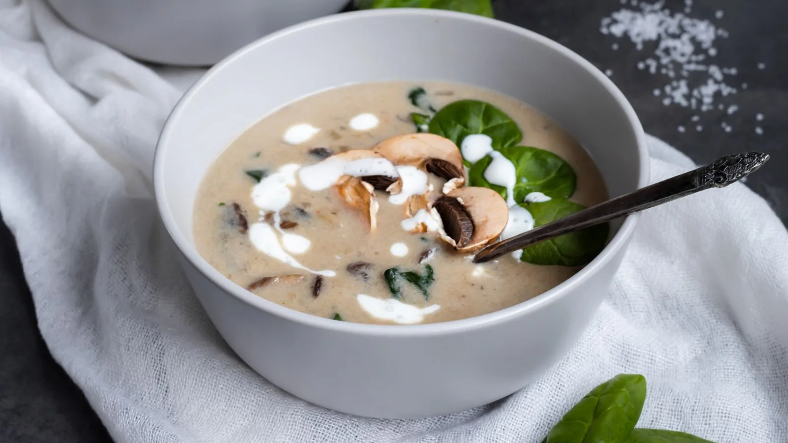 Delicious creamy mushroom soup garnished with fresh spinach leaves in a ceramic bowl.