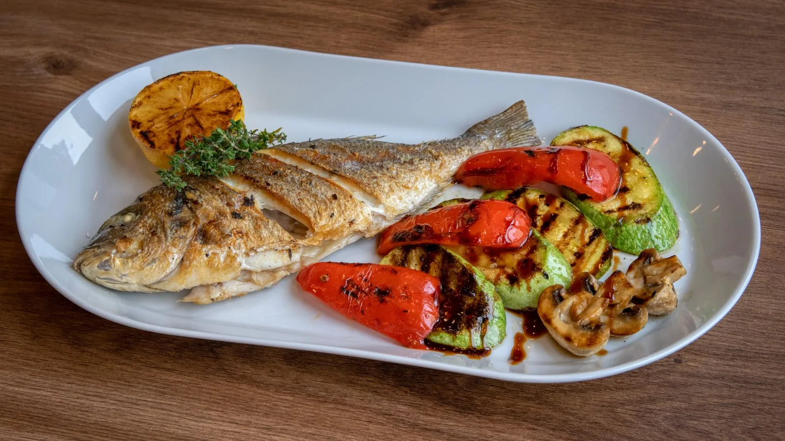 Grilled fish served with roasted vegetables on a ceramic plate.