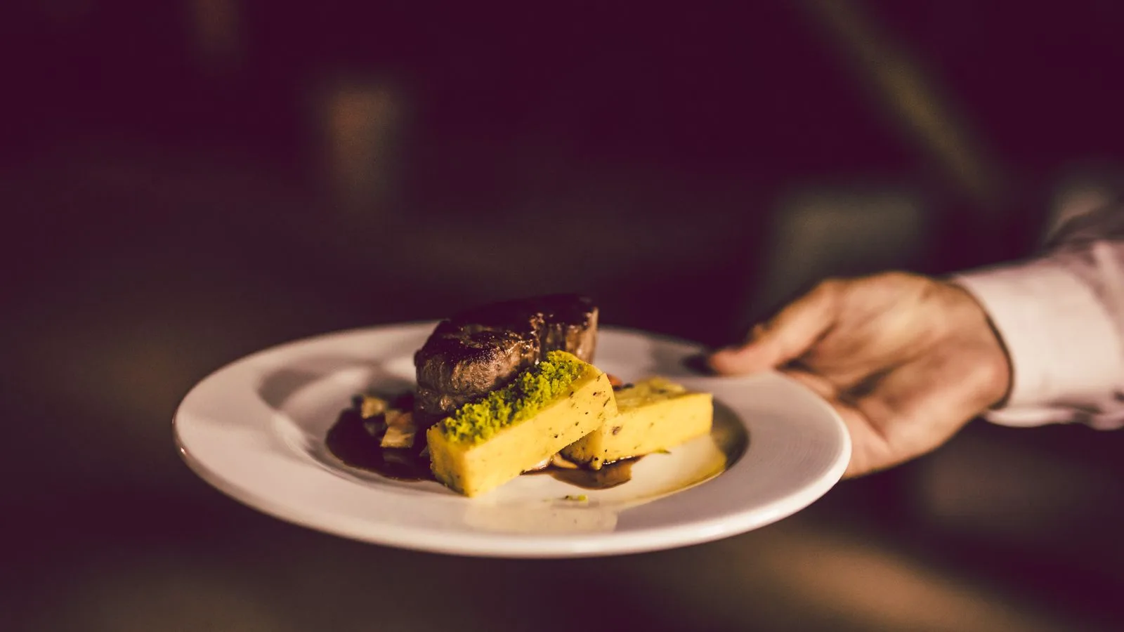 A gourmet meal elegantly plated and held by a hand, showcasing refined culinary art.