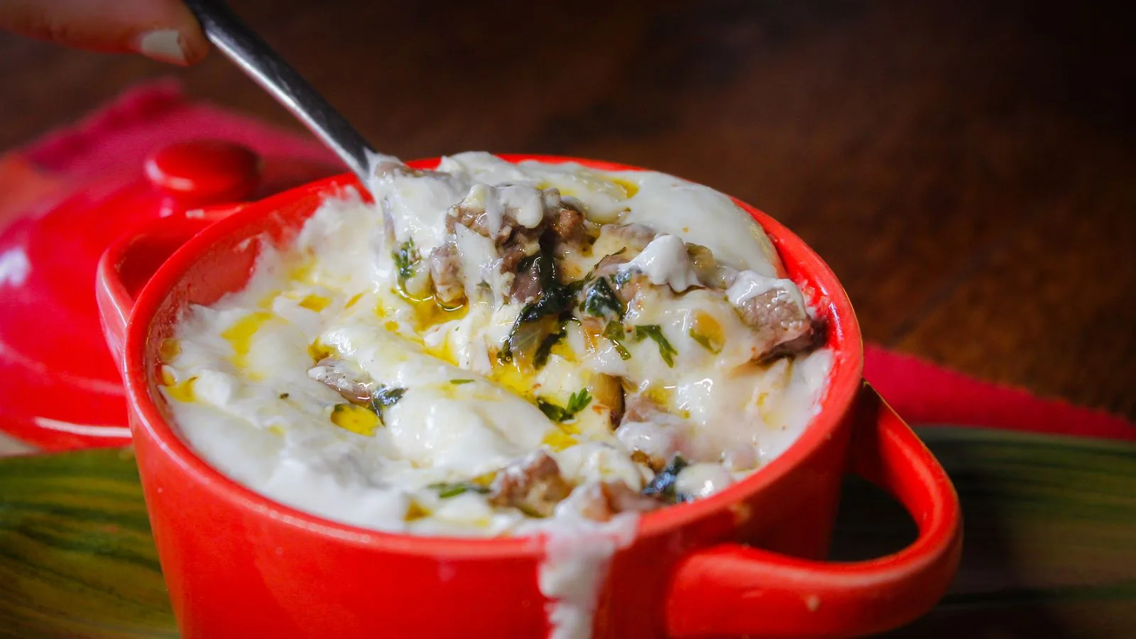 Savor this creamy cheese casserole with herbs, served hot in a vibrant red pot.