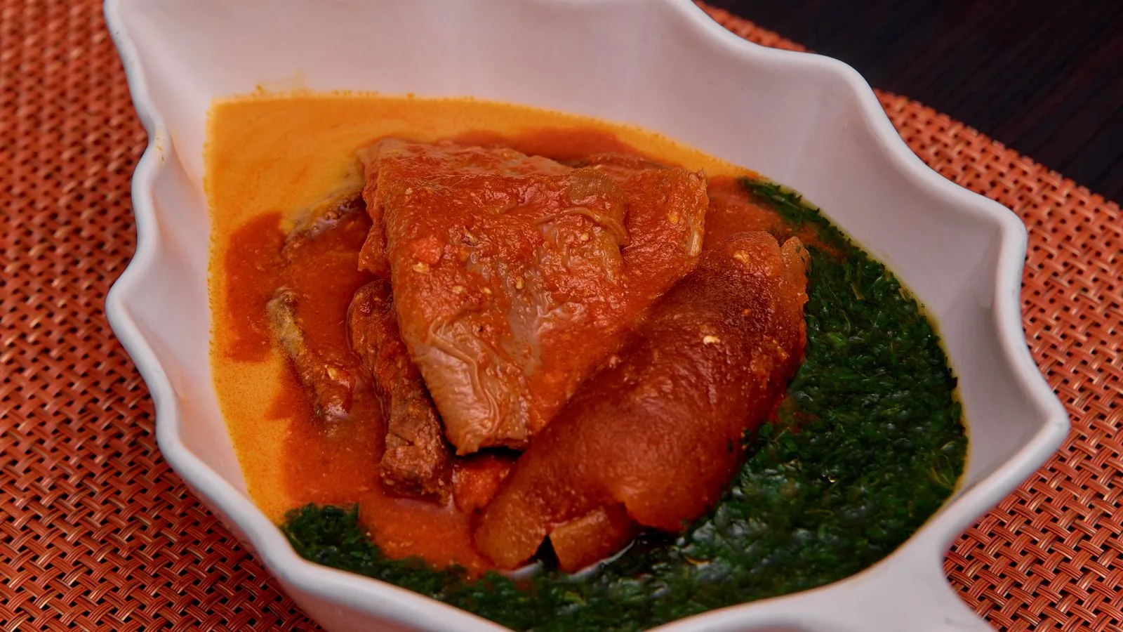 Leaf-shaped bowl with traditional African soup featuring meat and vegetables.