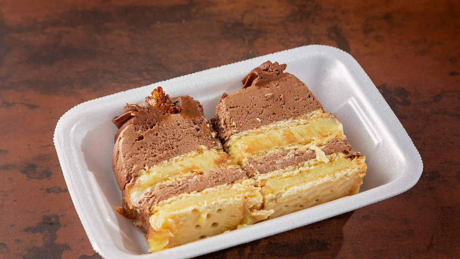 Delicious close-up of a chocolate and vanilla layer cake served in a Styrofoam tray.
