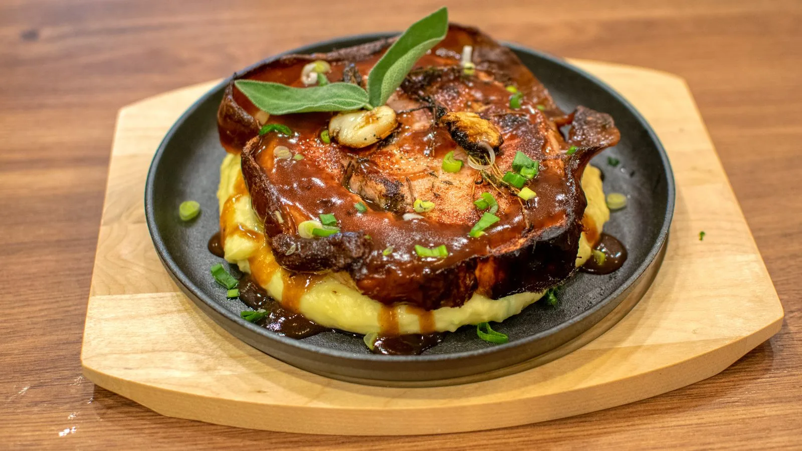 Juicy pork chop with mashed potatoes, sauce, and garnish on a black plate for a savory meal.