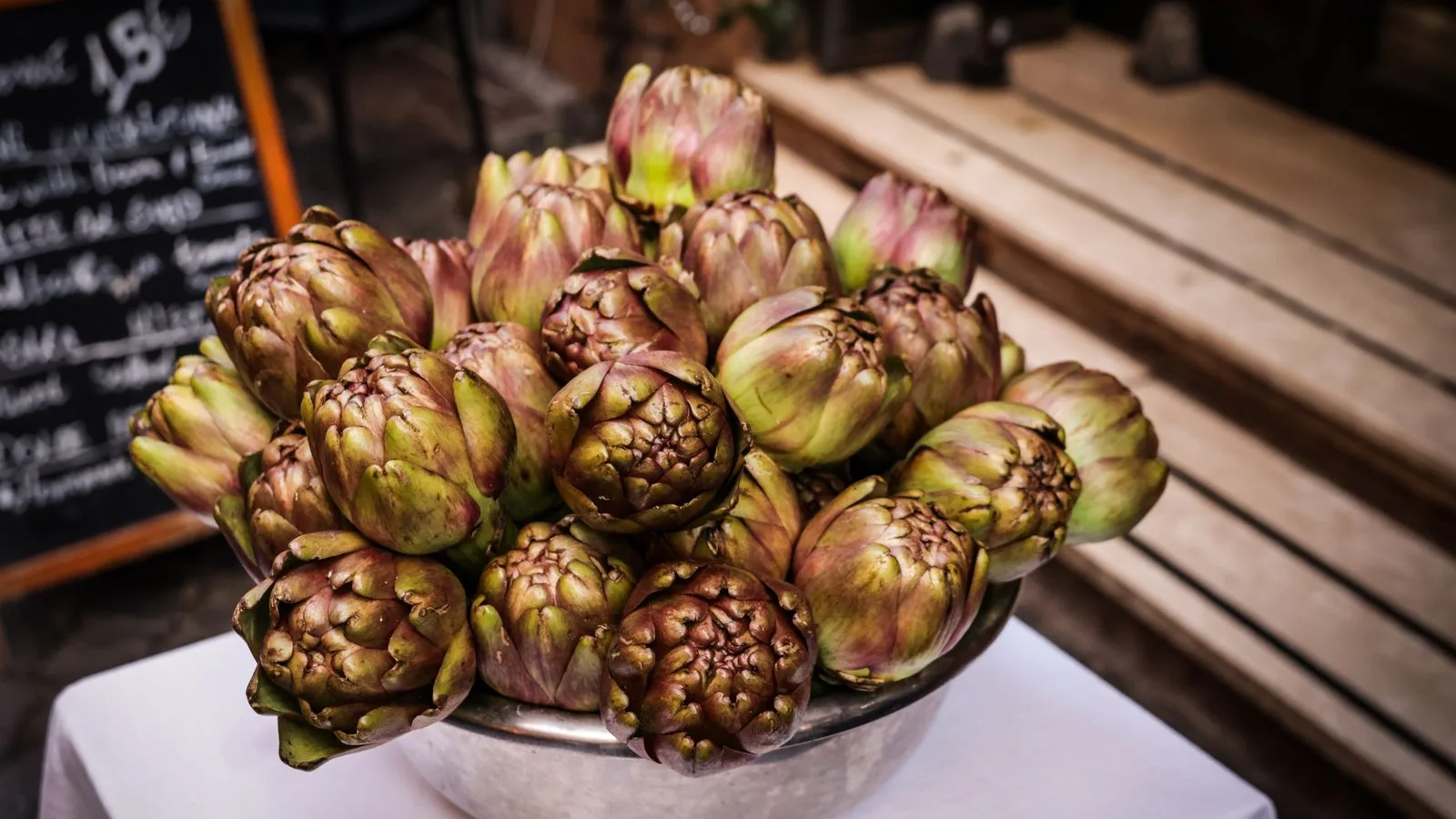 A large bowl of fresh artichokes displayed on a white tablecloth in a rustic setting, capturing their natural appeal.
