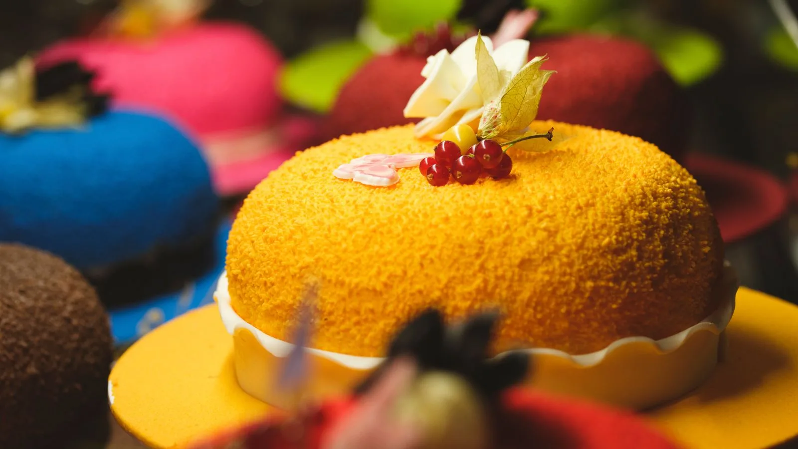 Vibrant display of assorted cakes adorned with fresh flowers and berries in a bakery.