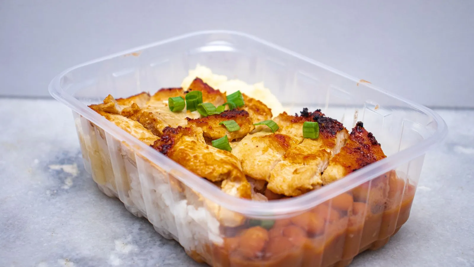 Delicious grilled chicken with beans and rice in a clear takeout container.