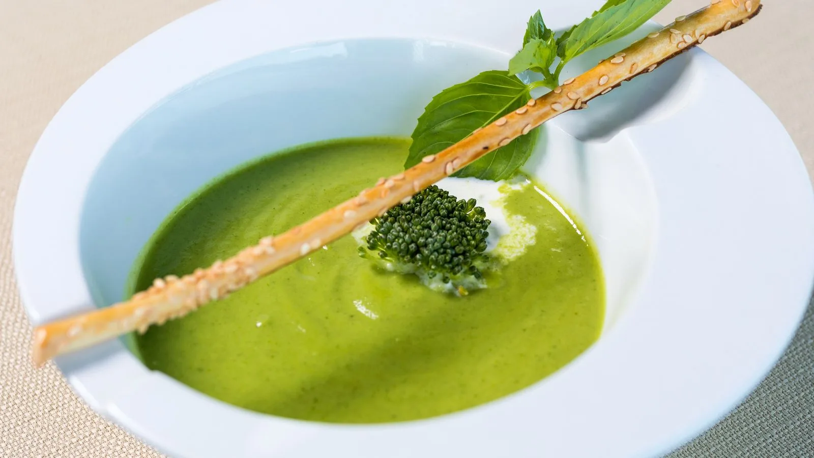 A bright green pea soup in a white bowl, garnished with croutons and herbs, elegantly presented.