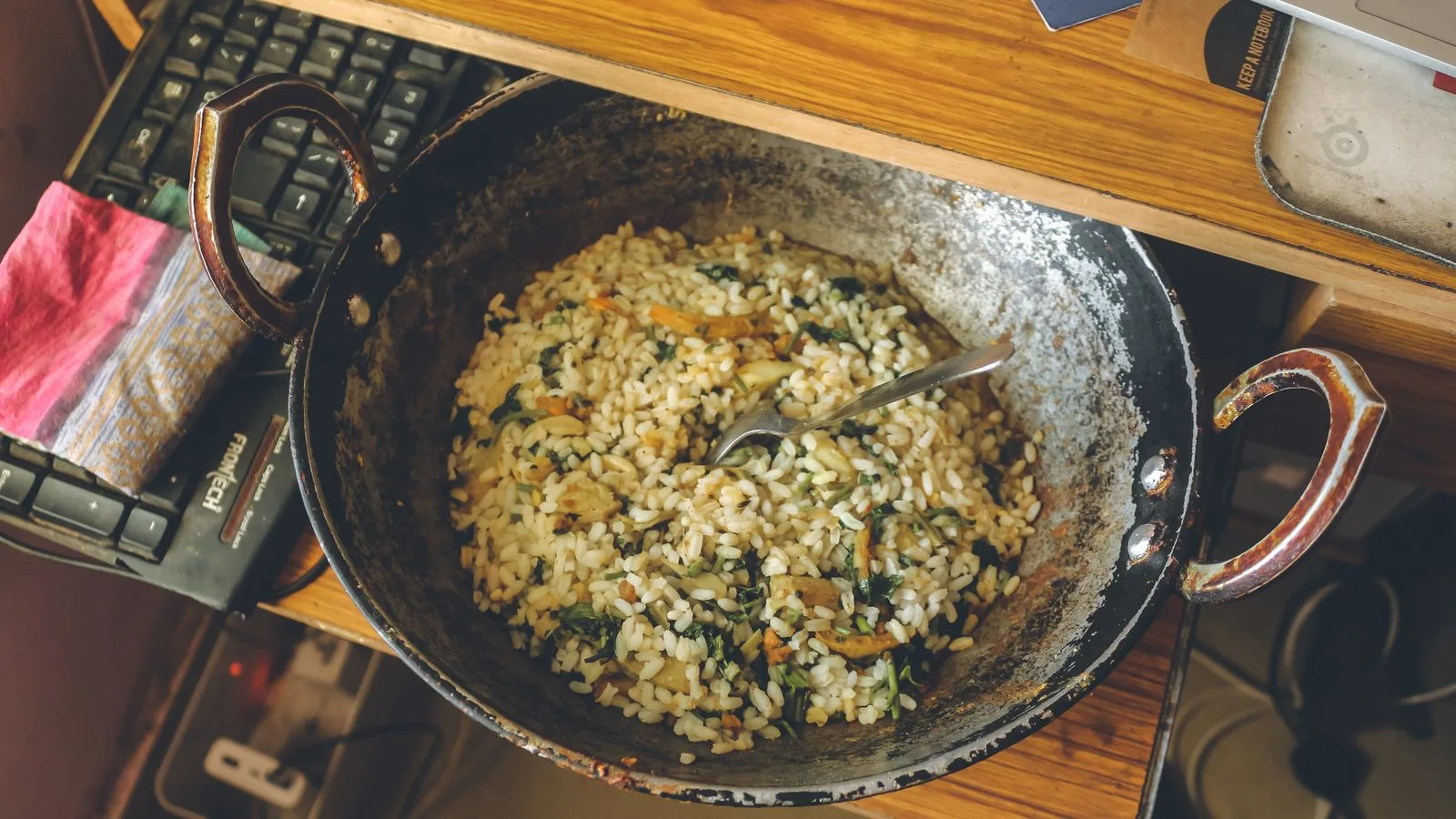 Top view of a cooked rice dish in a rustic pan on a wooden table with a keyboard nearby.