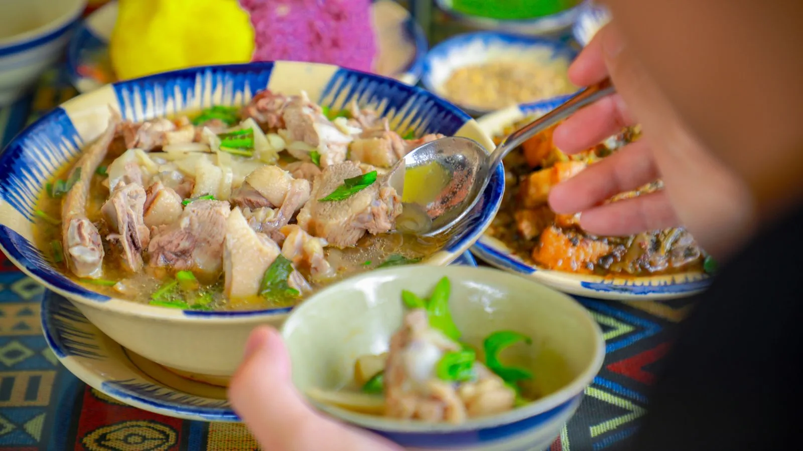 Close-up of a flavorful chicken soup being served at a vibrant dinner setup.