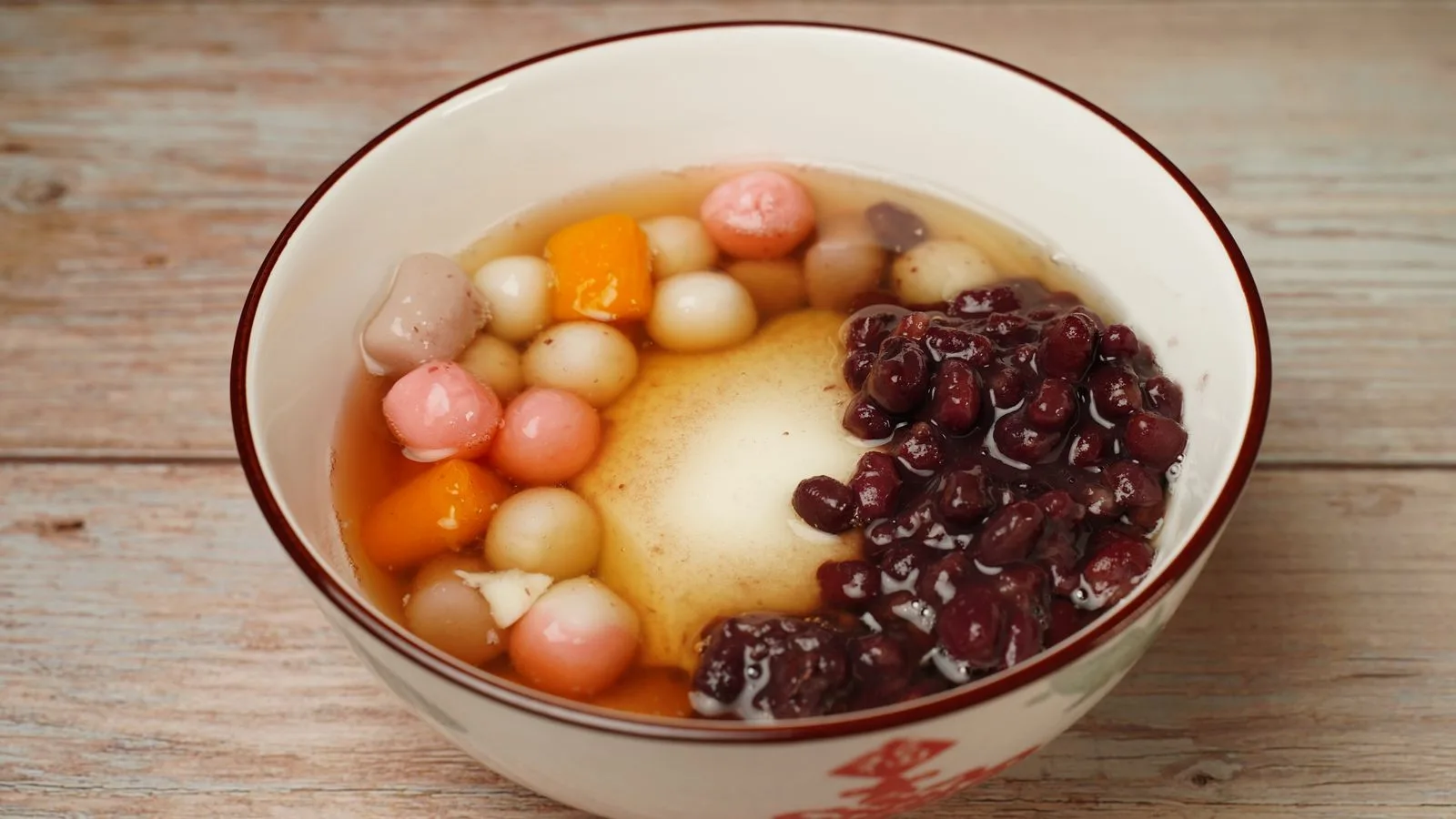 A colorful bowl of traditional sweet dessert featuring red beans and mochi balls.
