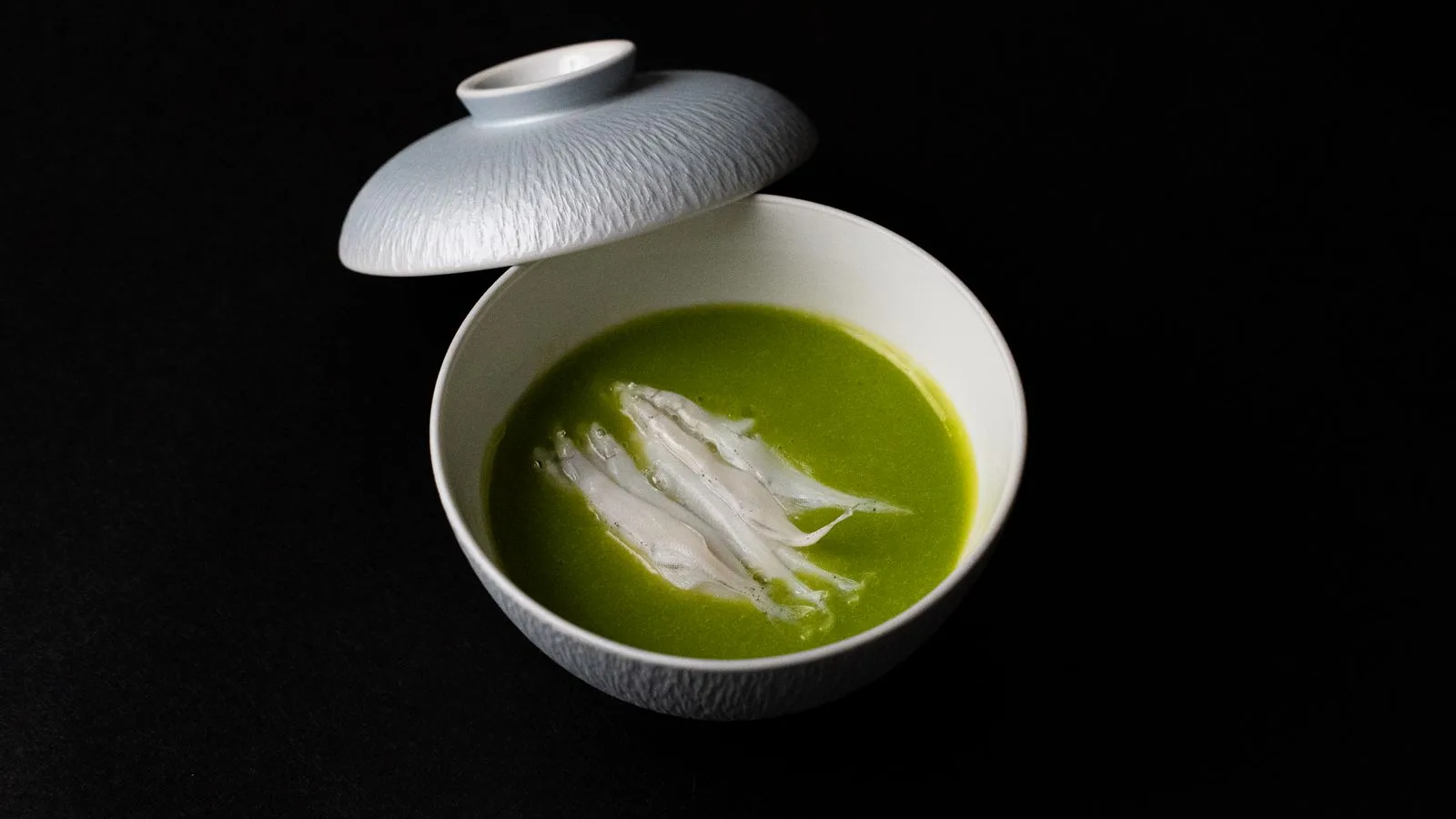 A stylish green soup with fish in a delicate Japanese ceramic bowl, captured from above.