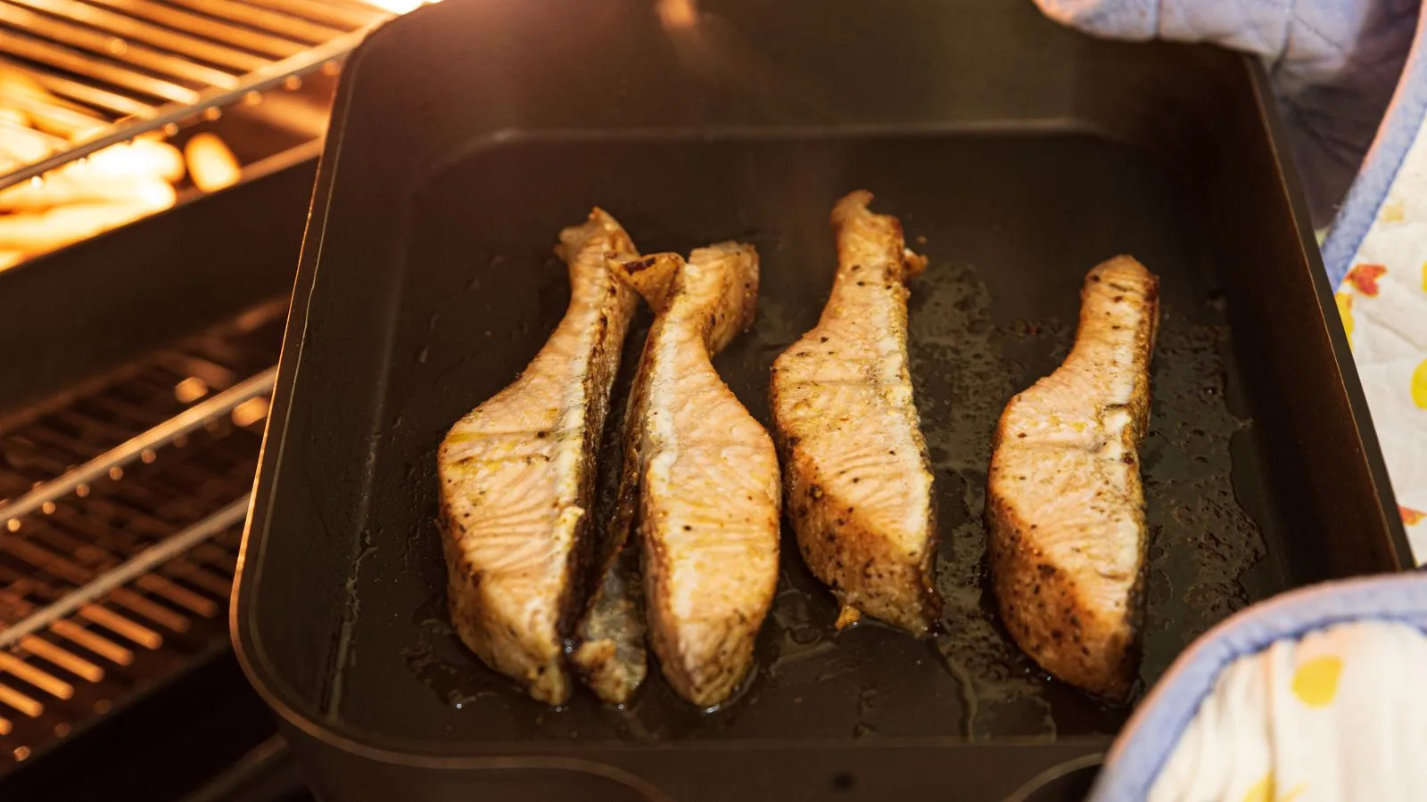 Close-up of four seasoned salmon fillets being baked in an oven with mitts.